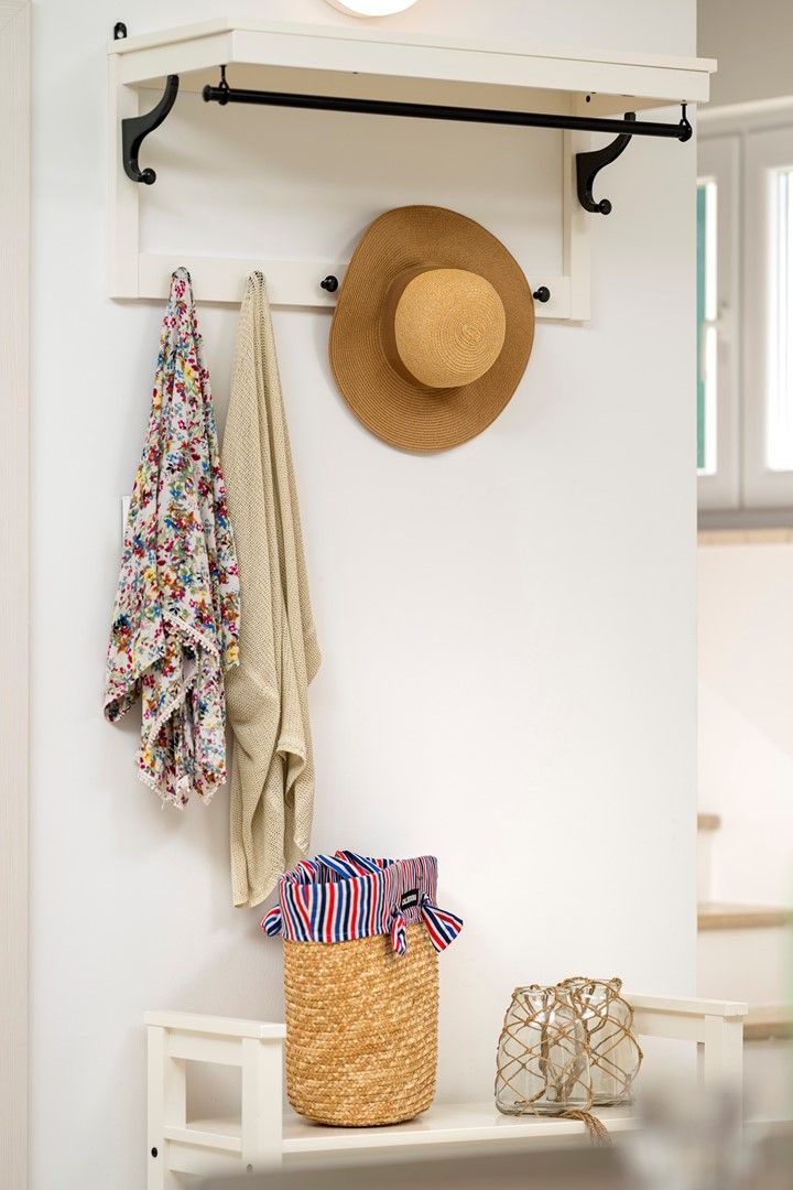 A white wall with a hat, a floral towel, and a striped bag hanging on a black metal rod.
