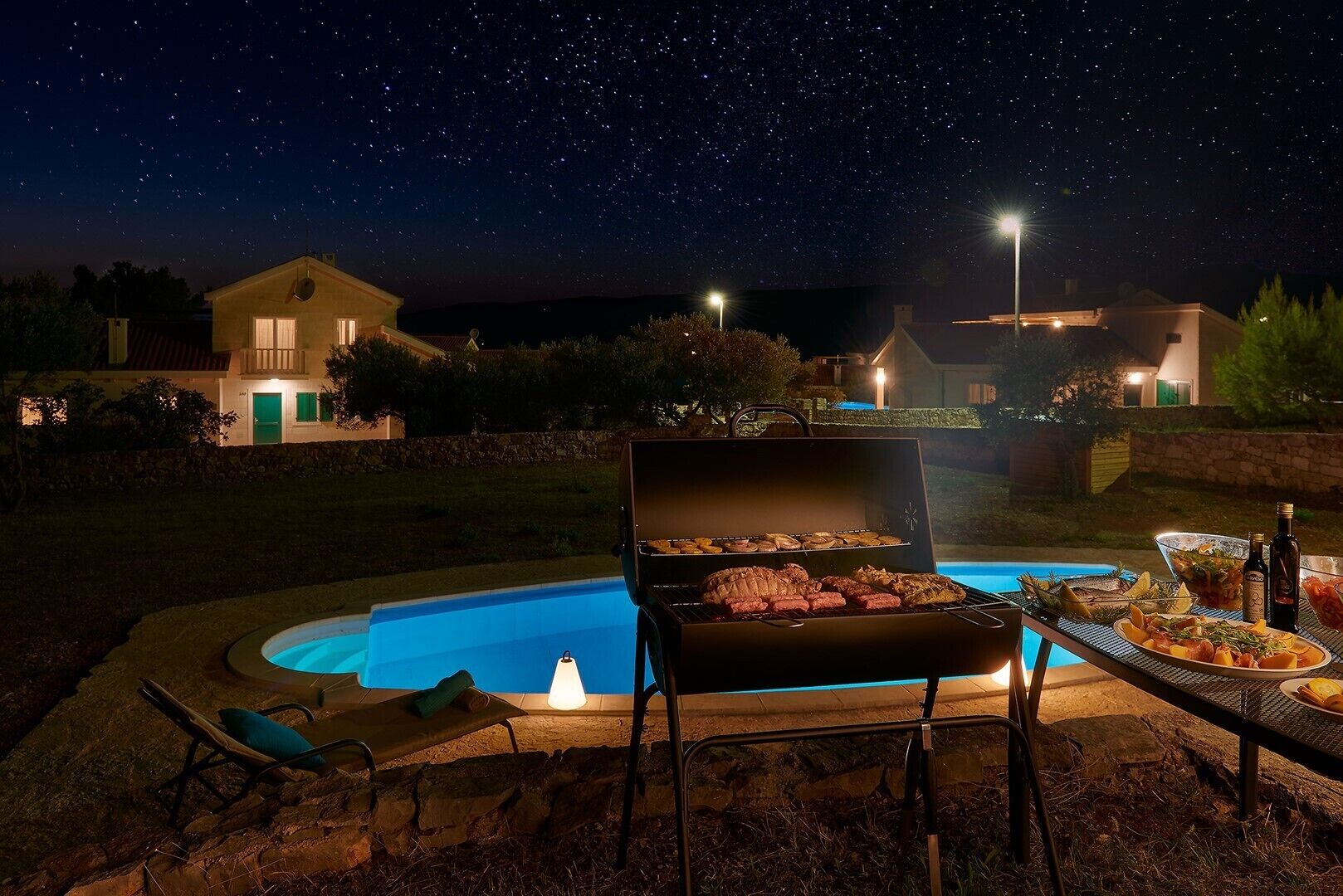 A backyard with a swimming pool, a barbecue grill, and a dining table set for an outdoor meal.