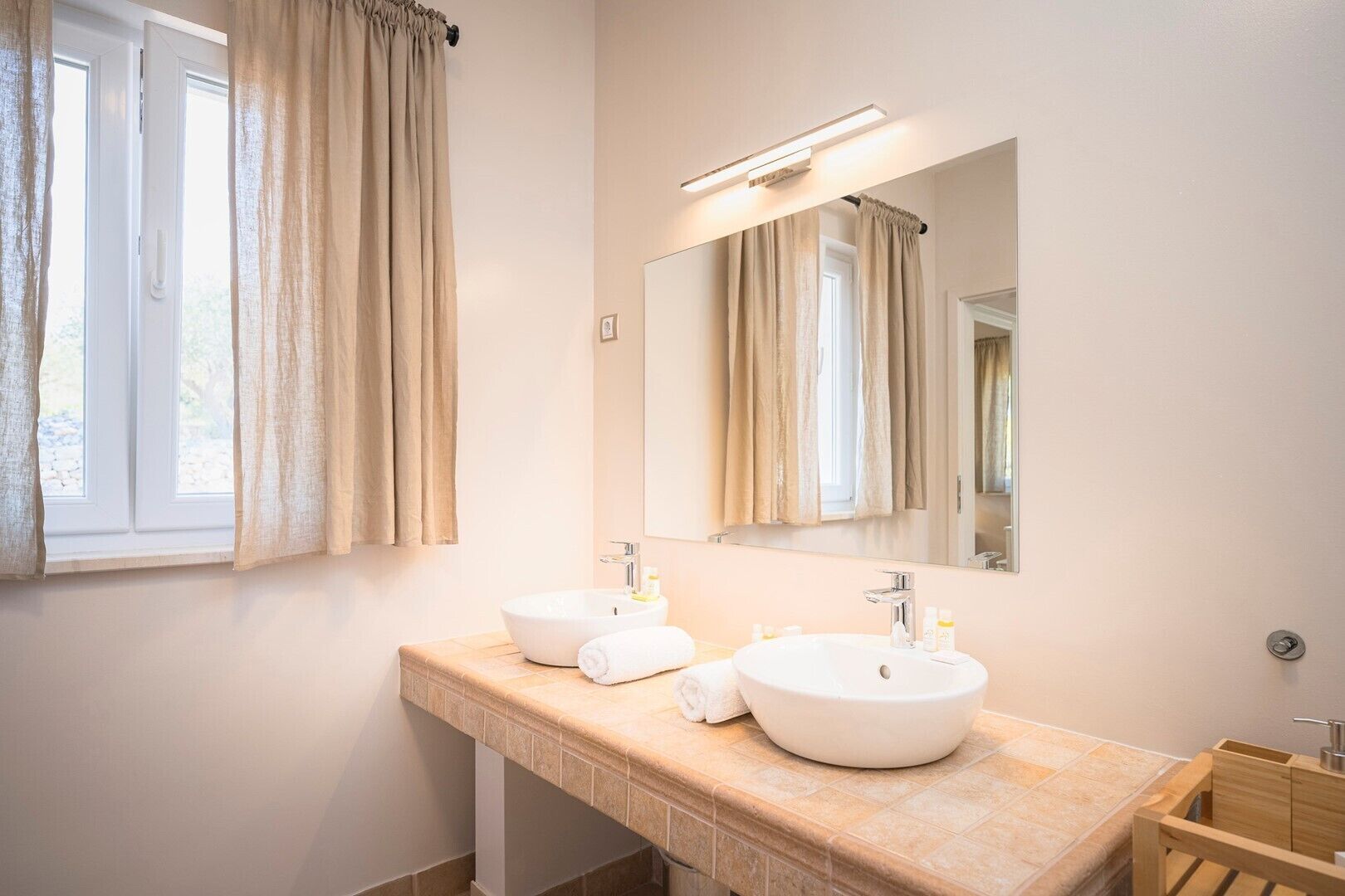 Ein Badezimmer mit zwei Waschbecken, einem großen Spiegel und einem Fenster mit Vorhängen.