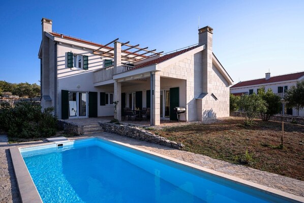 A modern two-story house with a swimming pool, outdoor seating, and a stone pathway leading to the entrance.