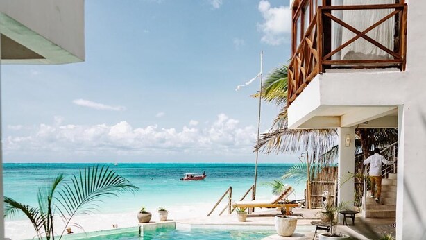 A pool area with a view of the ocean, a boat, and a building with a balcony. - ZAN Tropical Jambiani Beach (Jambiani)