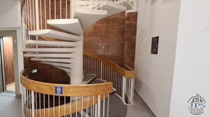 A spiral staircase with a wooden handrail and white railings, leading to a lower level.