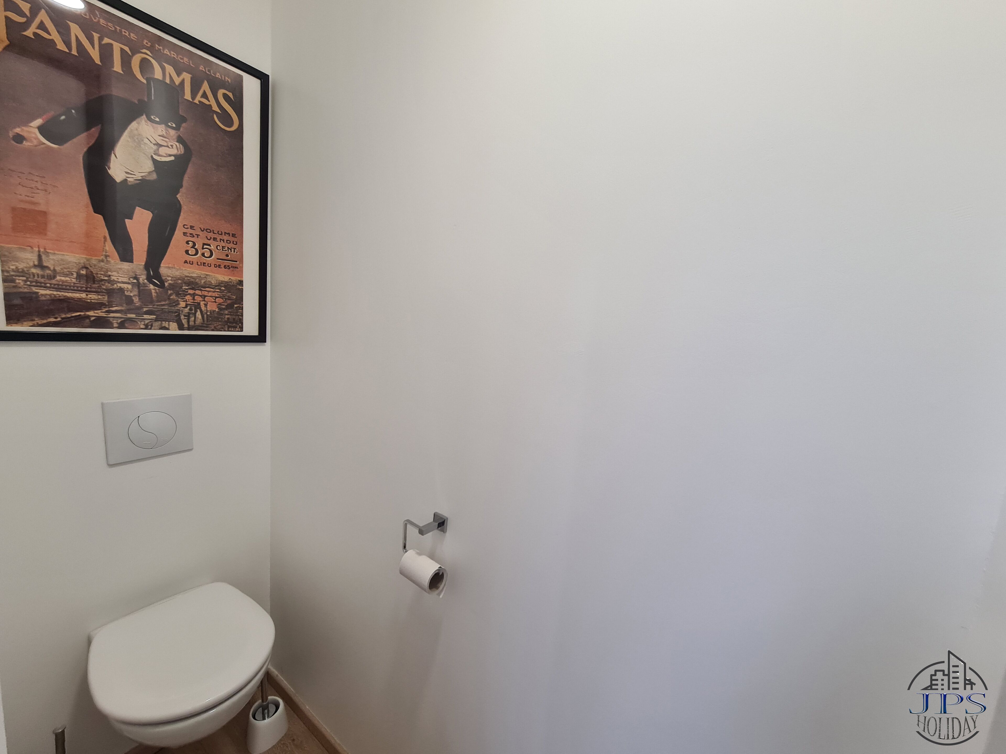 A bathroom with a toilet, a toilet paper holder, and a poster on the wall.