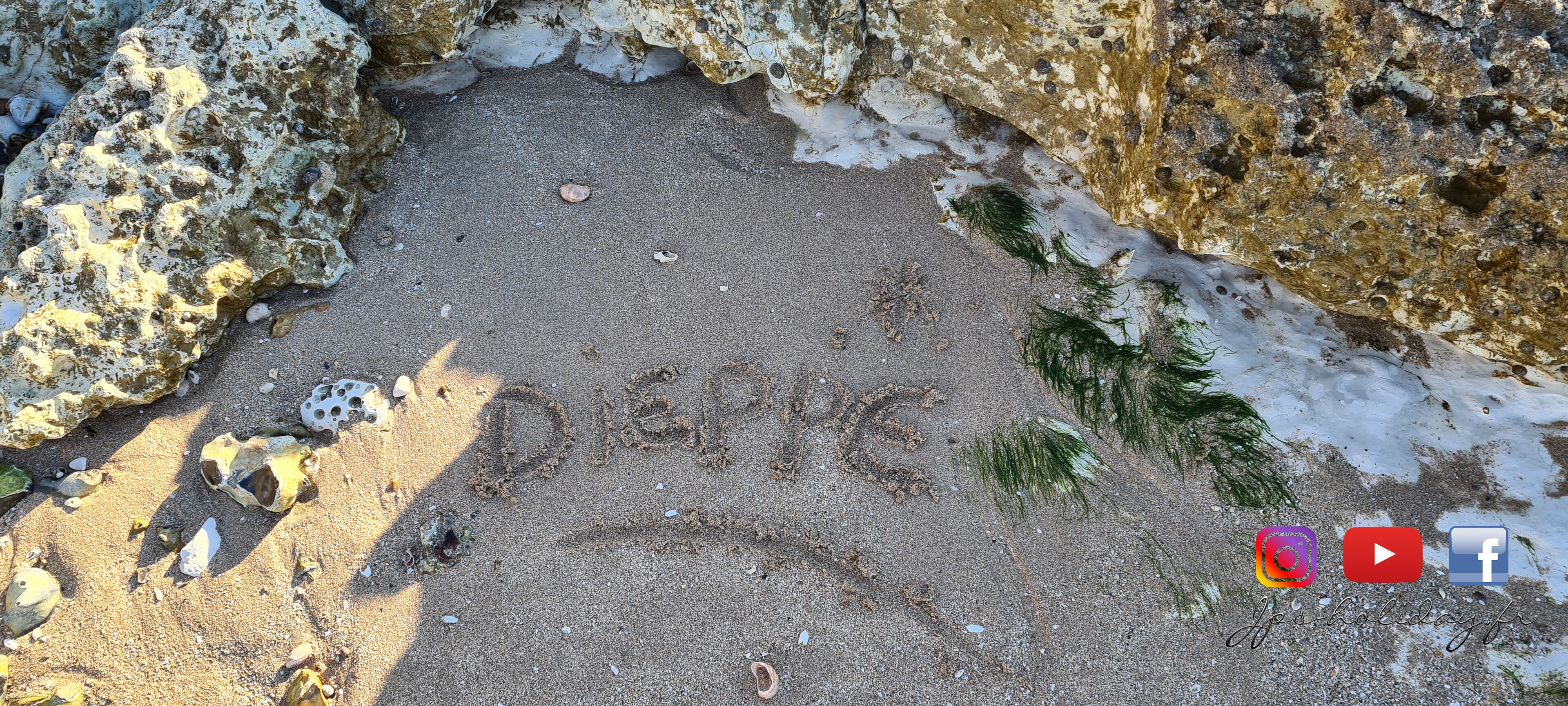 Een strand met het woord "DOLCE" in het zand, omgeven door rotsen en wier.