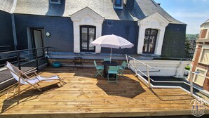 A wooden deck with a table and chairs, a white umbrella, and a pool.