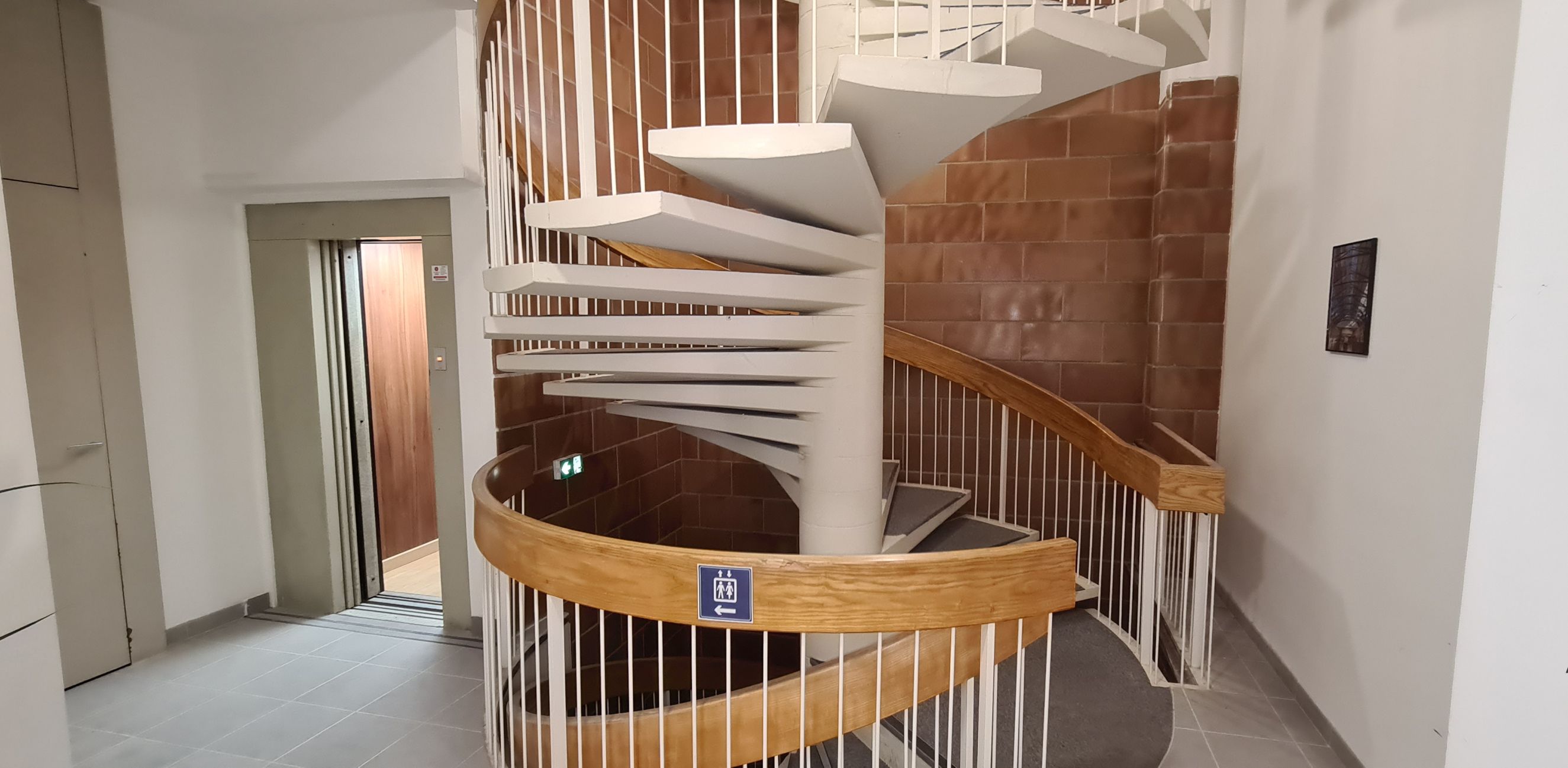A spiral staircase with a wooden handrail and white balustrades, leading to an upper floor.