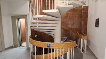 A spiral staircase with a wooden handrail and white balustrades, leading to an upper floor.