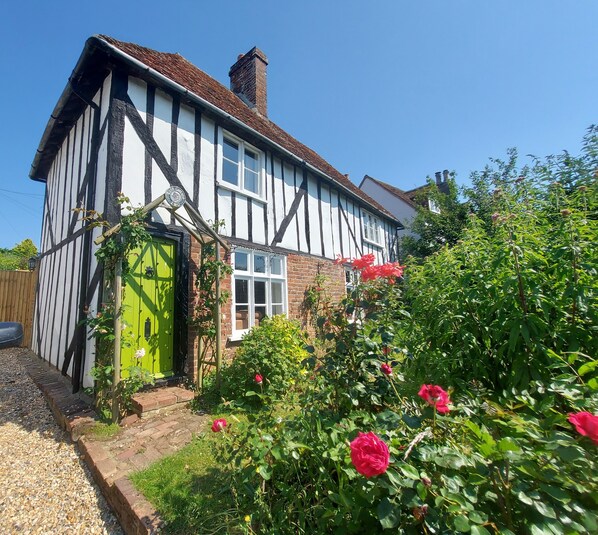 A traditional half-timbered house with a green door, surrounded by a garden with red flowers.