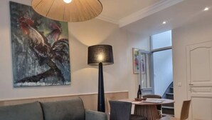 Ett vardagsrum med en soffa, ett bord med stolar, en lampa och en tavla som föreställer en tupp.