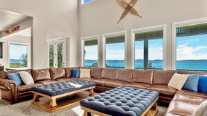A spacious living room with a large brown leather sectional sofa, two wooden ottomans, and a view of the ocean through large windows. - 7 acre Estate in Gated Reserve Community with Access to Pools, Beach, & Trails (Fish Haven)