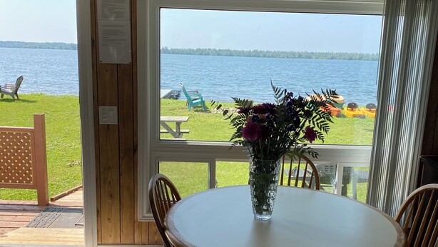 Een eetruimte met een ronde tafel en houten stoelen, met uitzicht op een meer en een houten terras buiten.