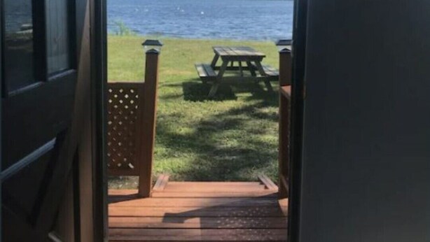 Eine offene Tür führt zu einer Terrasse mit einem Picknicktisch und Blick auf ein Gewässer.