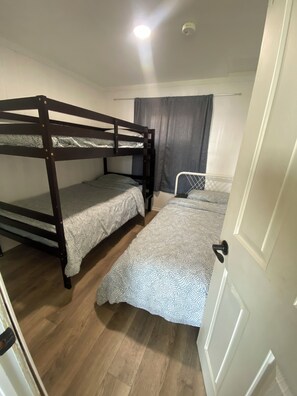 Una habitación con dos literas, una cama individual, una silla y una puerta.