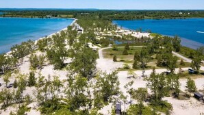 Eine Vogelperspektive auf ein Küstengrundstück mit Sandstrand, dichter Vegetation und blauem Himmel.