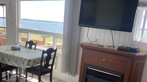 Un coin repas avec une table et des chaises, une cheminée, un téléviseur fixé au mur et une vue sur l’eau.