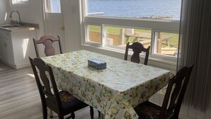 Un coin repas avec une table et des chaises, une vue sur le lac, et une cuisine équipée d’un évier et de placards.