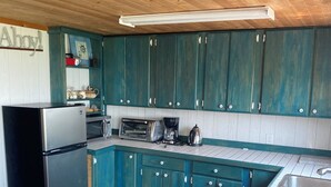 Een compacte keuken met blauwgroene kastjes, een koelkast, een magnetron, een broodrooster en een koffiezetapparaat.