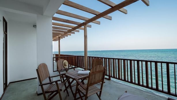 A balcony with wooden furniture, a table, and a chair, overlooking the sea. - Pili Pili Family (Jambiani)