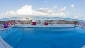 A pool with a wooden deck and lounge chairs, overlooking a beach with boats and a clear sky. - Pili Pili Family (Jambiani)