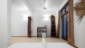 A spacious room with a large bed, a wooden ladder, a shelf with items, and a door with curtains. - Pili Pili Family (Jambiani)