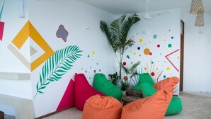 A room with colorful bean bags, a large plant, and a wall with geometric and abstract designs. - Pili Pili Family (Jambiani)