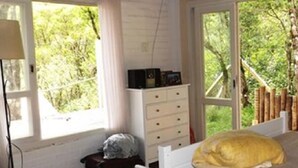A bedroom with a bed, a dresser, and a window with a view of trees. - Beautiful single-story house, super cozy: 3 suites. (Monte Verde)