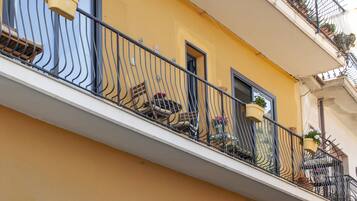 Un balcone con parete gialla, ringhiera in ferro battuto nero e piante in vaso.