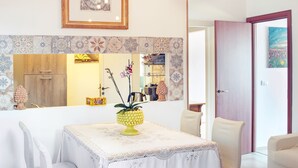 Un comedor con una mesa preparada para dos, un jarrón decorativo con flores, una obra de arte enmarcada sobre la mesa y un salpicadero de azulejos estampados.
