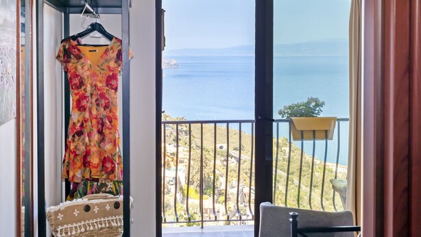 Una habitación con vista al mar, un vestido colgado y una cesta de mimbre.