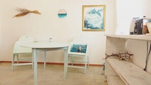 Una stanza con un tavolo rotondo e due sedie, un quadro astratto incorniciato e una mensola con un ramo.