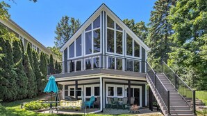 Ein zweistöckiges Haus mit überdachter Terrasse, einer Treppe und einem gepflegten Rasen.
