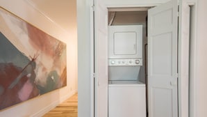 A laundry room with a washer and dryer, a painting on the wall, and a wooden floor.