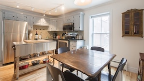 A modern kitchen with stainless steel appliances, a wooden dining table, and a large window providing natural light.