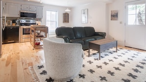 A modern kitchen with stainless steel appliances, a dining area with a leather couch, and a patterned rug.