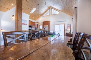 A spacious kitchen with wooden cabinets, a large dining table, and a high ceiling with skylights.