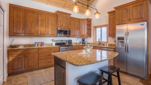 Una cocina con armarios de madera, encimeras de granito, electrodomésticos de acero inoxidable y una isla central con taburetes.