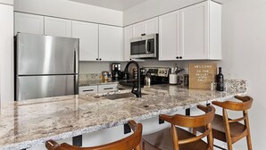 A modern kitchen with white cabinets, stainless steel appliances, a granite countertop, and a bar area with wooden chairs. - The Valley Vista: Top floor unit w/ views & hot tub (Telluride)