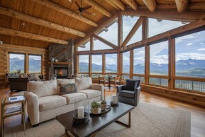 Un salon spacieux doté d’une cheminée, de grandes fenêtres offrant une vue sur les montagnes et d’un coin salon confortable.