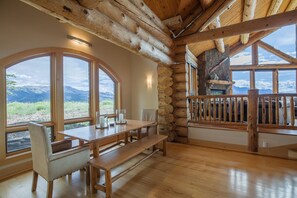 A log cabin interior with a wooden dining table, benches, and large windows offering mountain views. - 140 Serapio Ln (Telluride)