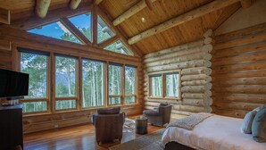 Ein Schlafzimmer in einer Blockhütte mit einem großen Bett, zwei Sesseln, einem Fernseher und einem Kamin.