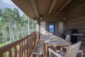 A wooden deck with a table and chairs, a grill, and a view of tall trees. - 140 Serapio Ln (Telluride)