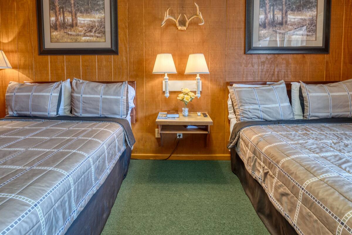 A hotel room with two beds, a nightstand with lamps, and framed pictures on the wall.