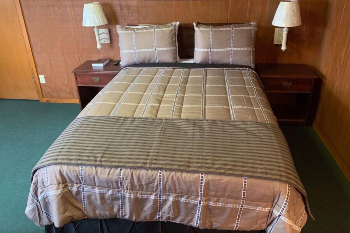 A hotel room with a large bed, two bedside tables, two wall-mounted lamps, and a framed picture on the wall.