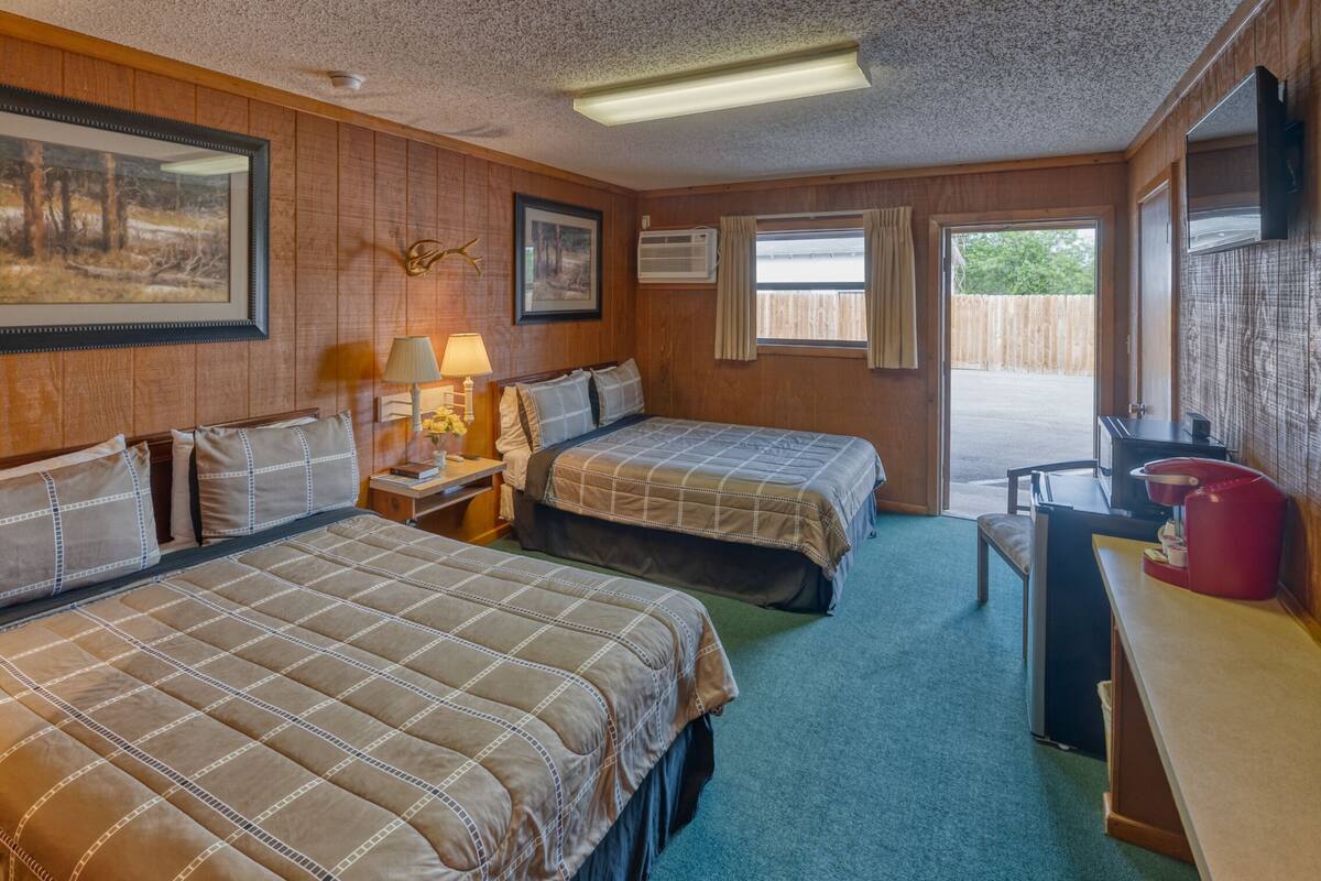 A room with two beds, a desk, a chair, a lamp, and a window.