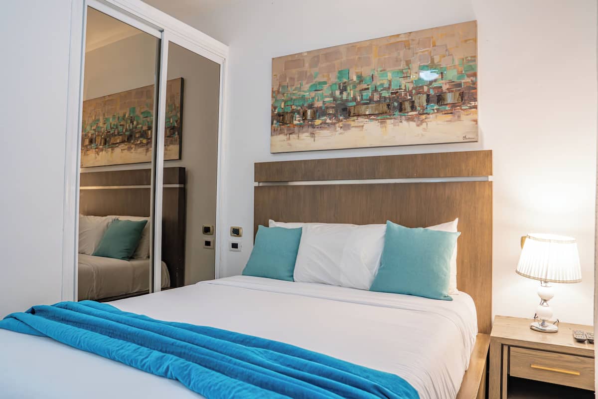 A hotel room with a bed, a nightstand, a lamp, a painting on the wall, and a sliding door leading to a bathroom.