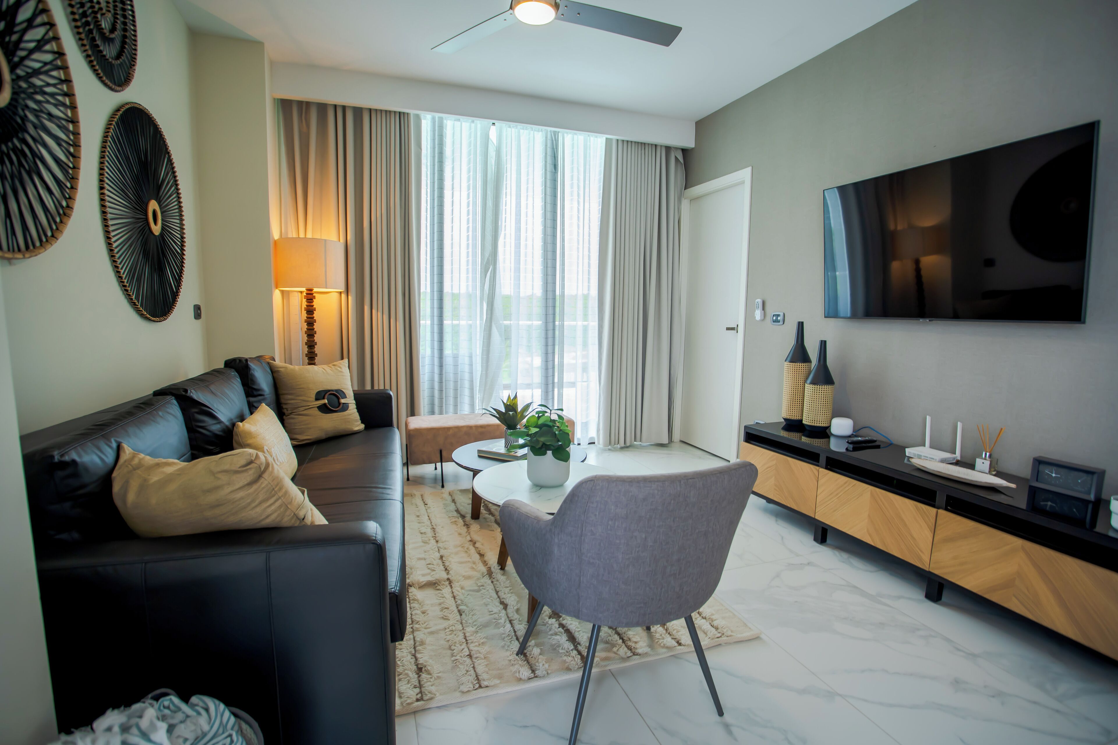 A modern living room with a black leather sofa, a grey armchair, a coffee table, and a TV mounted on the wall.