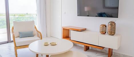 A modern living room with a white sofa, a round table with two plates, a TV mounted on the wall, and a wooden cabinet with decorative vases.