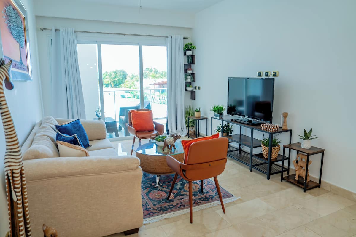 A living room with a sofa, chairs, a coffee table, a TV, and a balcony with plants.