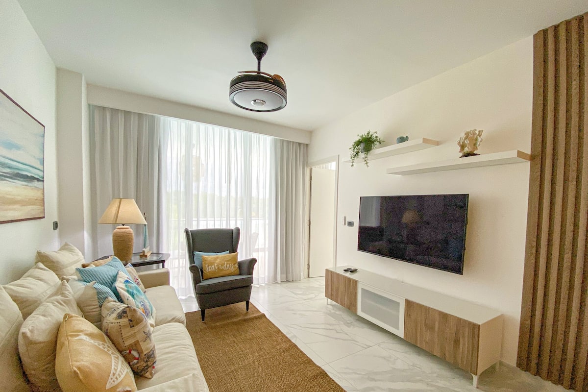 A modern living room with a sofa, a chair, a TV, and a ceiling fan.