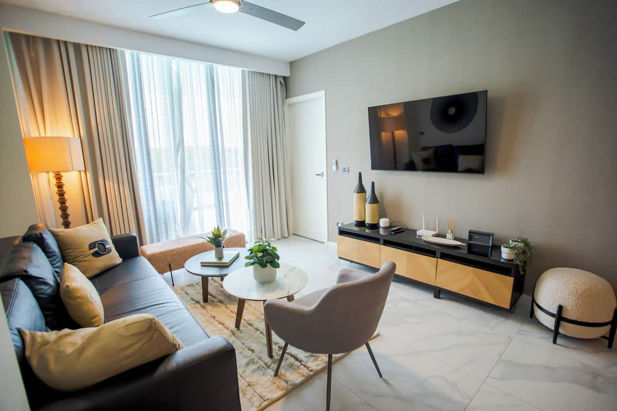A modern living room with a sofa, coffee table, and ottoman. There is a television mounted on the wall and a cabinet with decorative items.